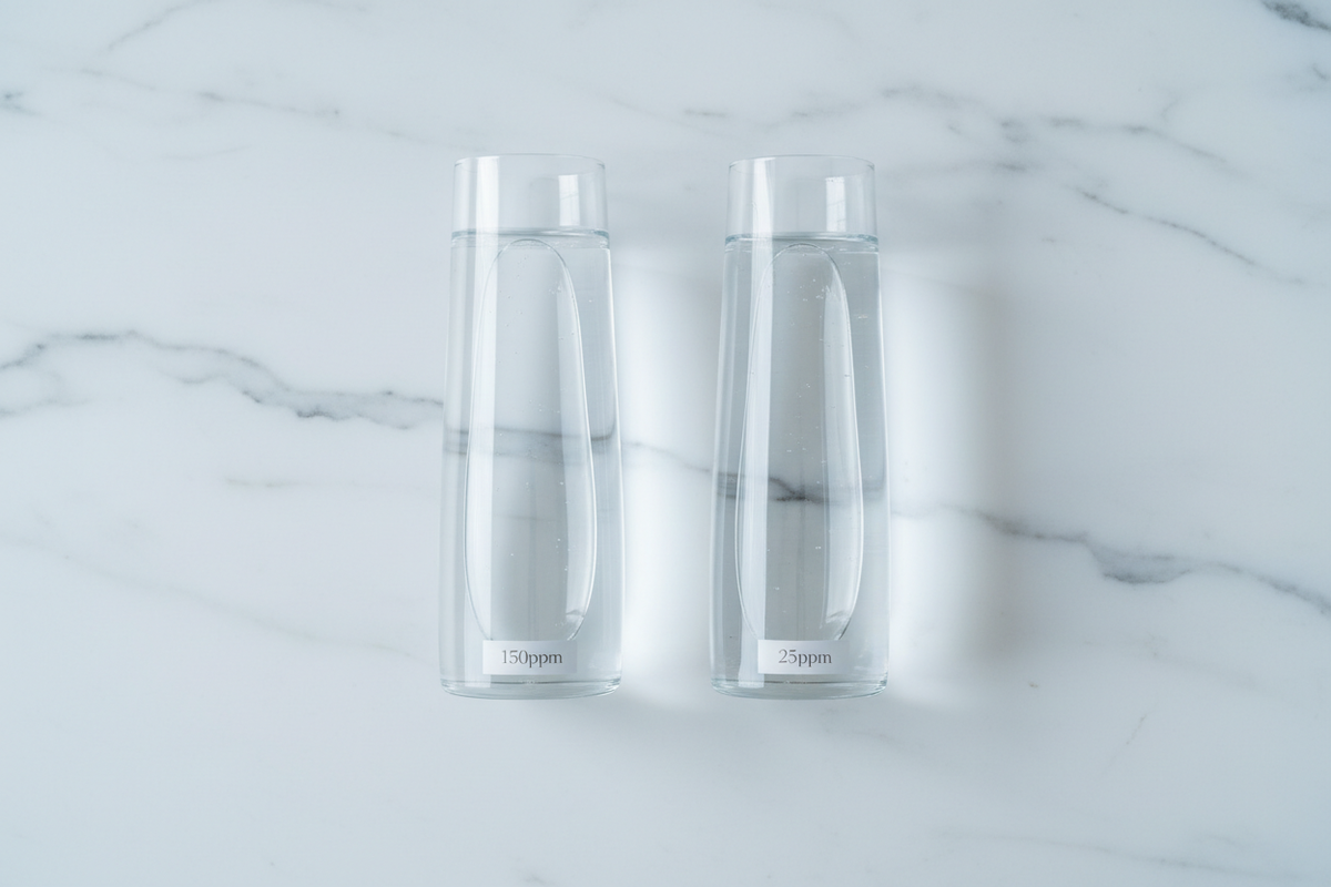 Two identical glass vessels of water side by side on a white marble surface, comparing regular water at 150ppm deuterium with Yavelle deuterium-depleted water at 25ppm